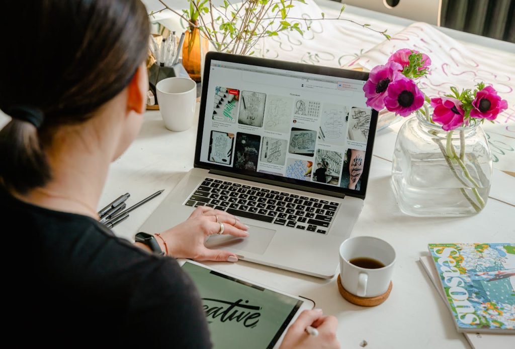 Woman in a creative workspace using a laptop and tablet for calligraphy. Artistic and tech-driven environment.